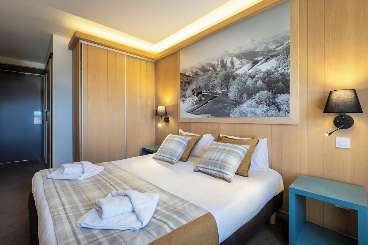 A hotel room with a large bed, two bedside tables, a wall-mounted lamp, and a framed picture of a snowy landscape.