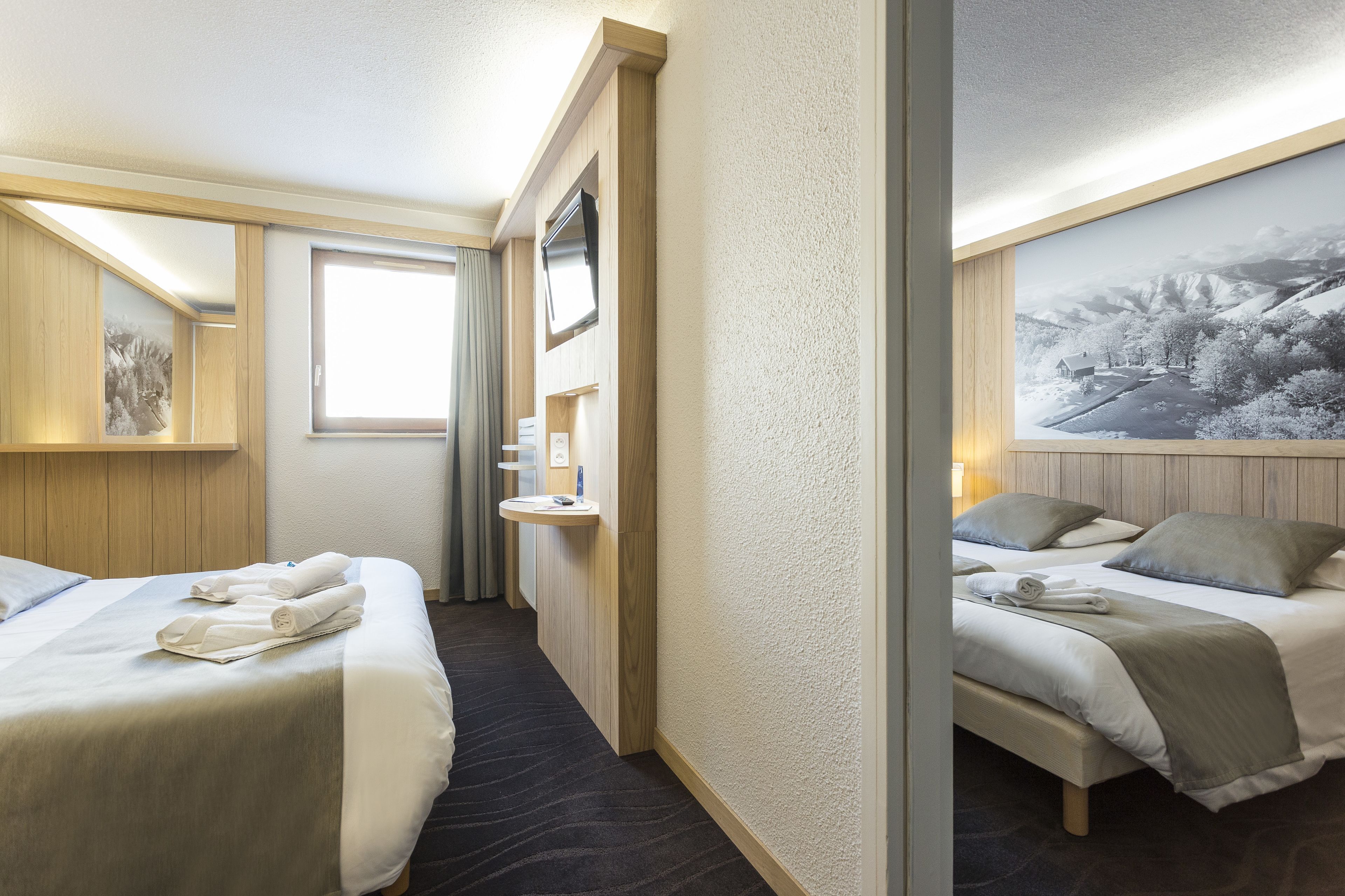 A hotel room with two beds, a bathroom with a sink, and a large window.