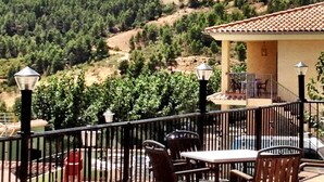 A terrace with outdoor furniture, a building with a tiled roof, and a mountainous backdrop. - Residencial Turístico Vega-Sierra (Bogarra)