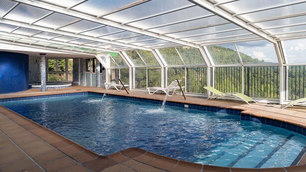 An indoor swimming pool with a glass ceiling, surrounded by lounge chairs and a view of a forested hillside. - Residencial Turístico Vega-Sierra (Bogarra)