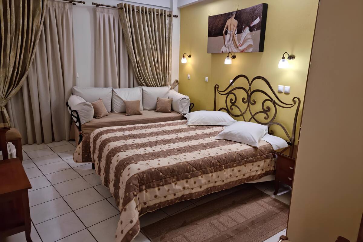A bedroom with two beds, beige curtains, a painting on the wall, and wall-mounted lights.