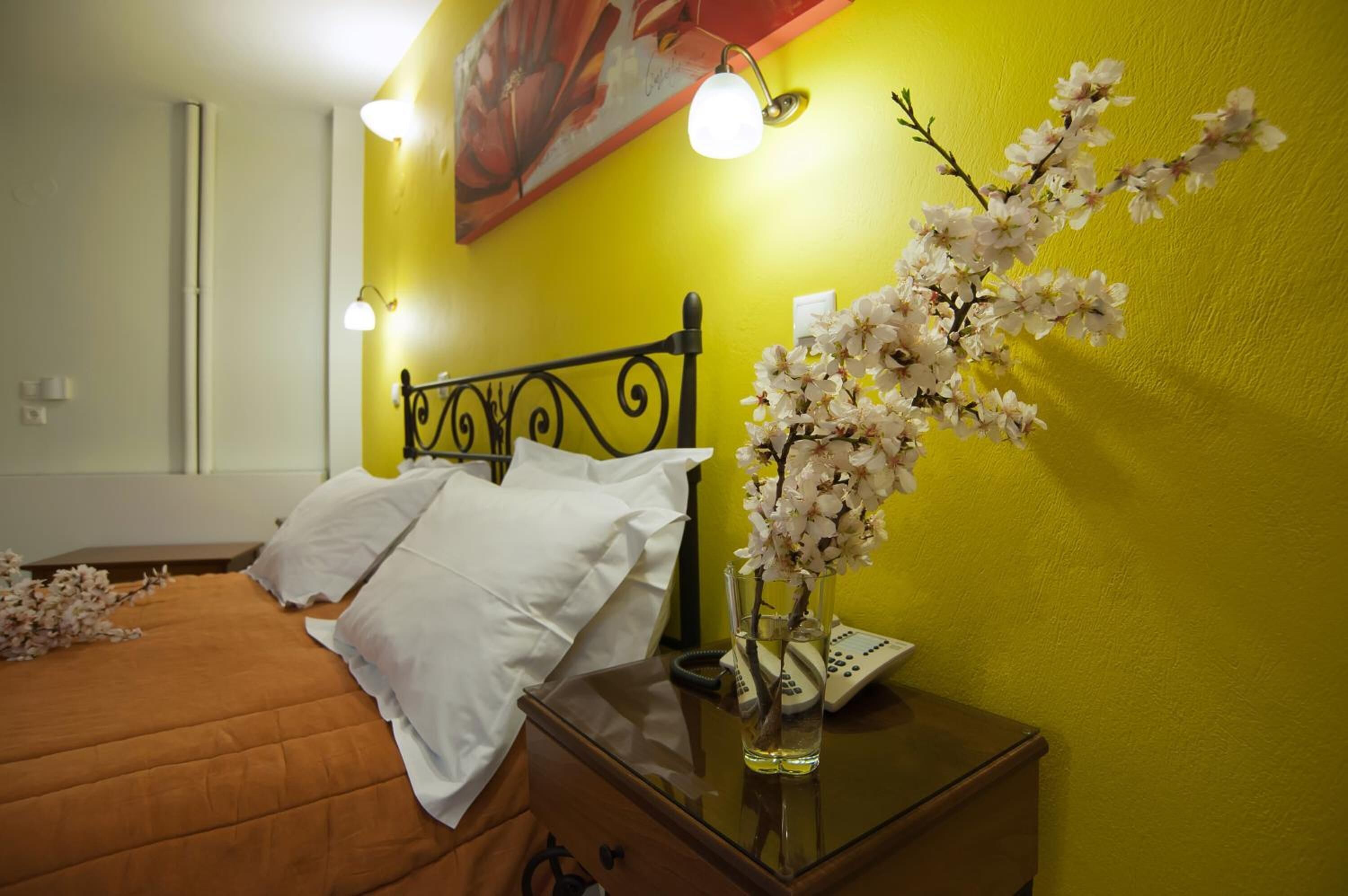 A hotel room with a bed, a bedside table with a vase of flowers, a telephone, and a painting on the wall.
