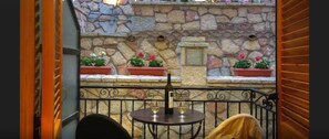 A stone wall with potted plants and a table with two wine glasses and a bottle.