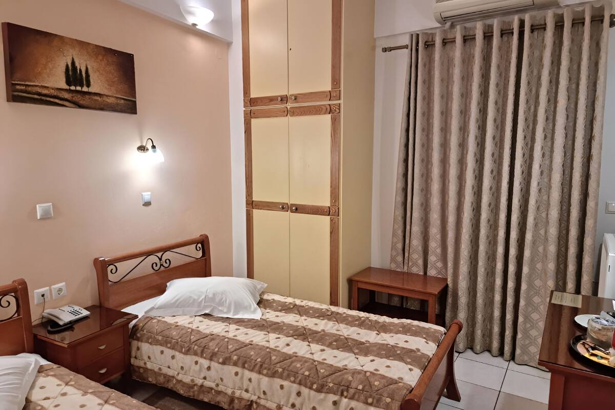 A bedroom with two beds, a wooden wardrobe, a bedside table with a phone, and a painting on the wall.