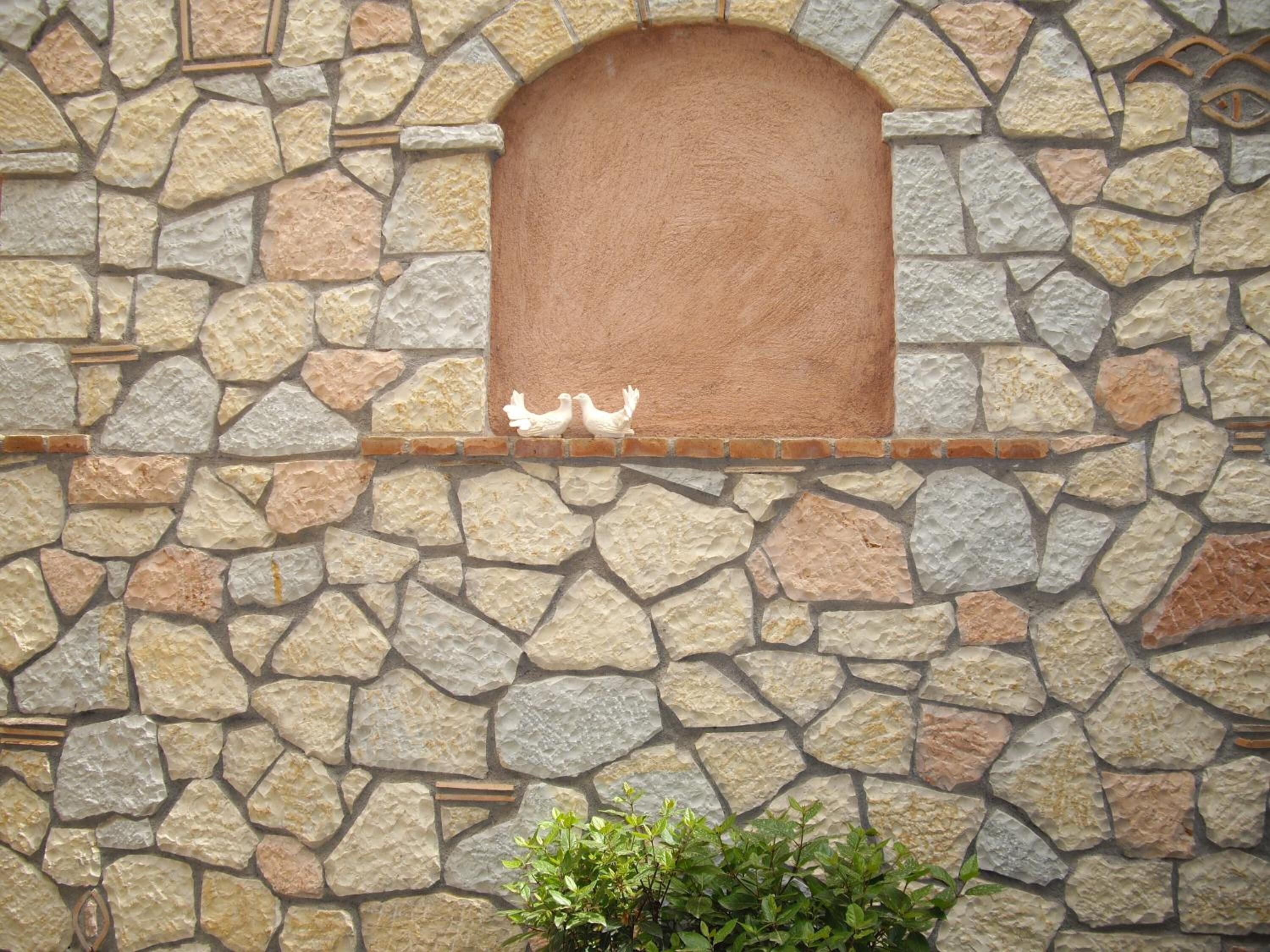 A stone wall with a decorative window and two white bird sculptures.