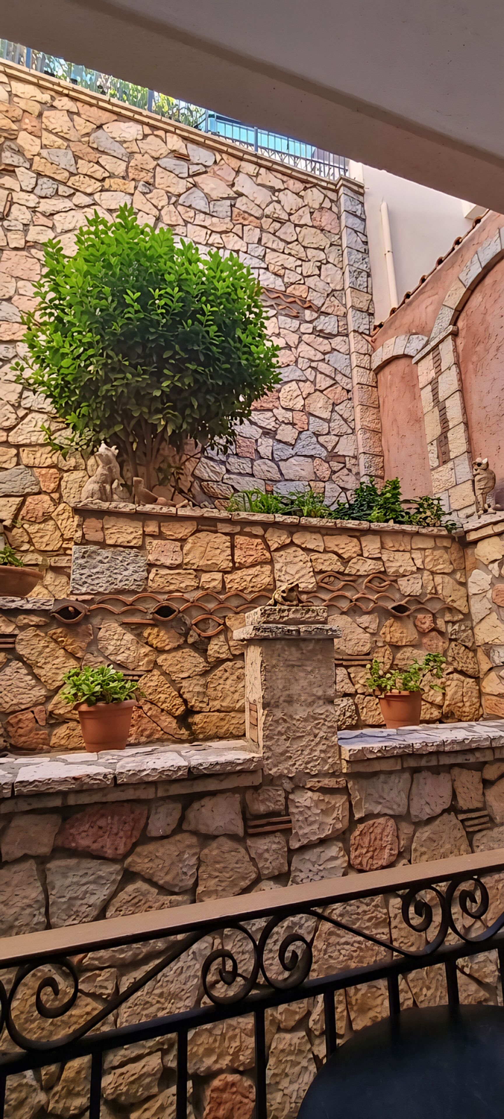A stone wall with a potted plant and a small fountain.