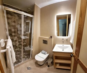 A bathroom with a glass-enclosed shower, a toilet, and a sink with a mirror above it.
