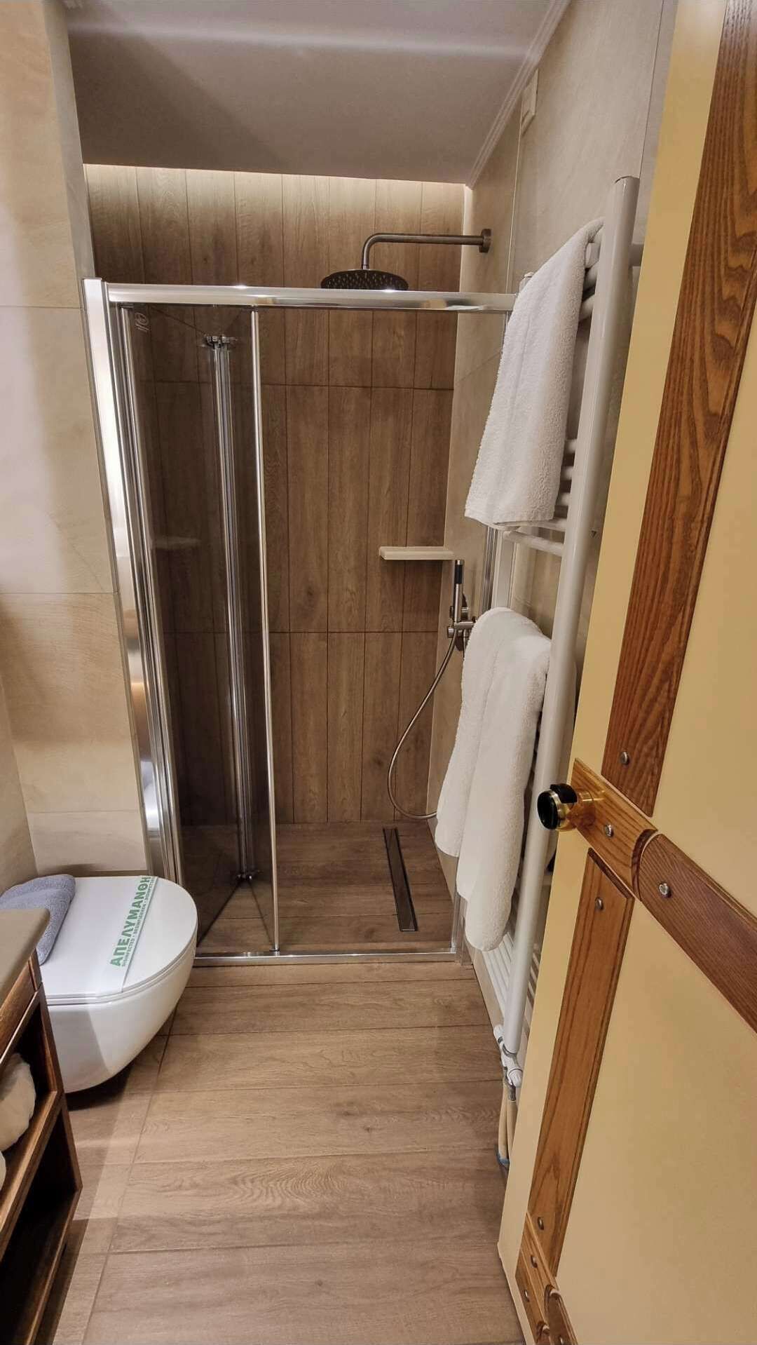 Une douche avec une porte en verre, des toilettes blanches et un plancher en bois.