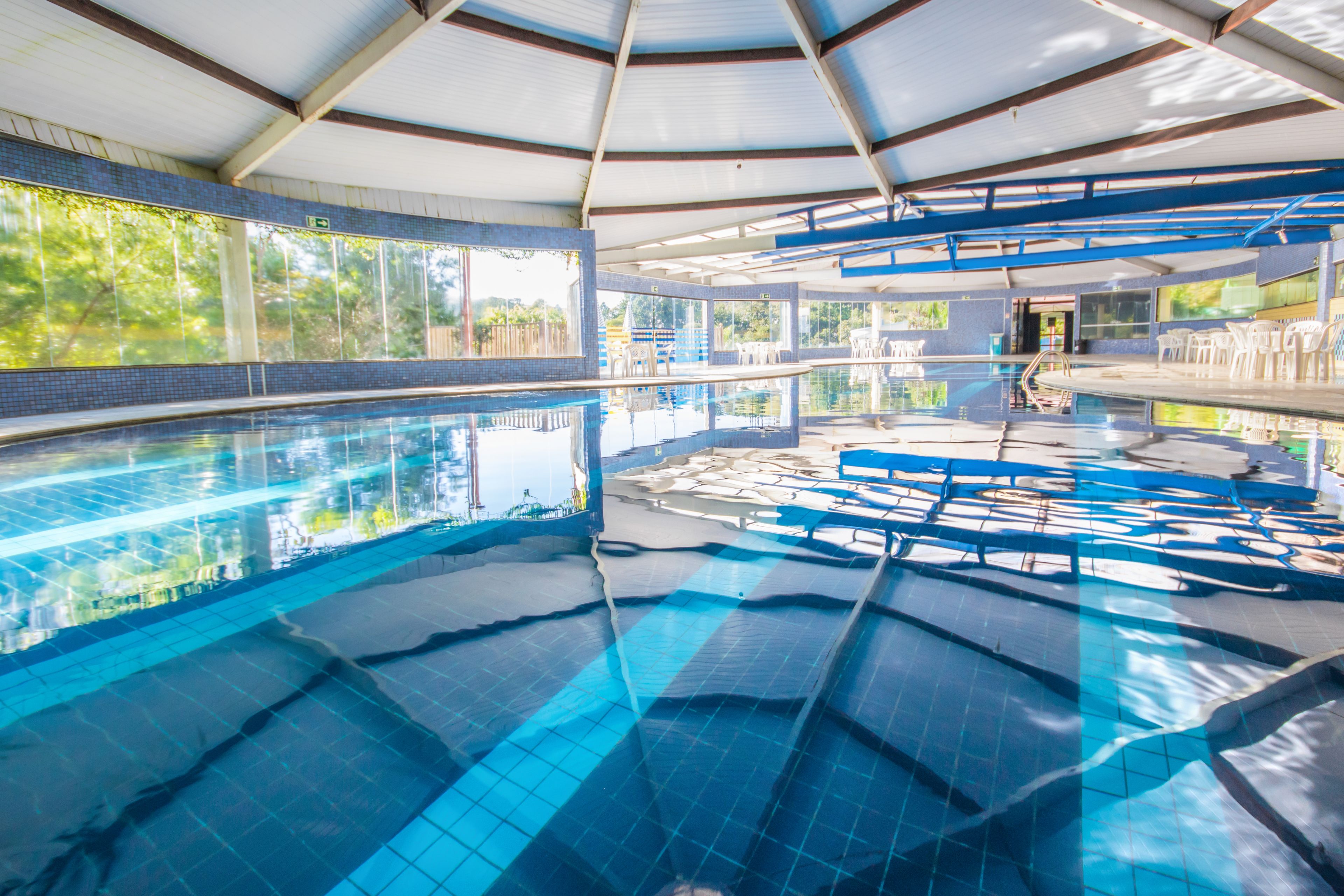 Piscina interna com água azul cristalina, paredes azulejadas e estrutura coberta.