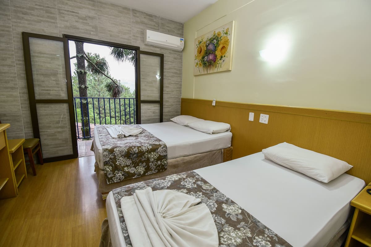 Quarto de hotel com duas camas, piso de madeira, varanda com vista e ar condicionado na parede.