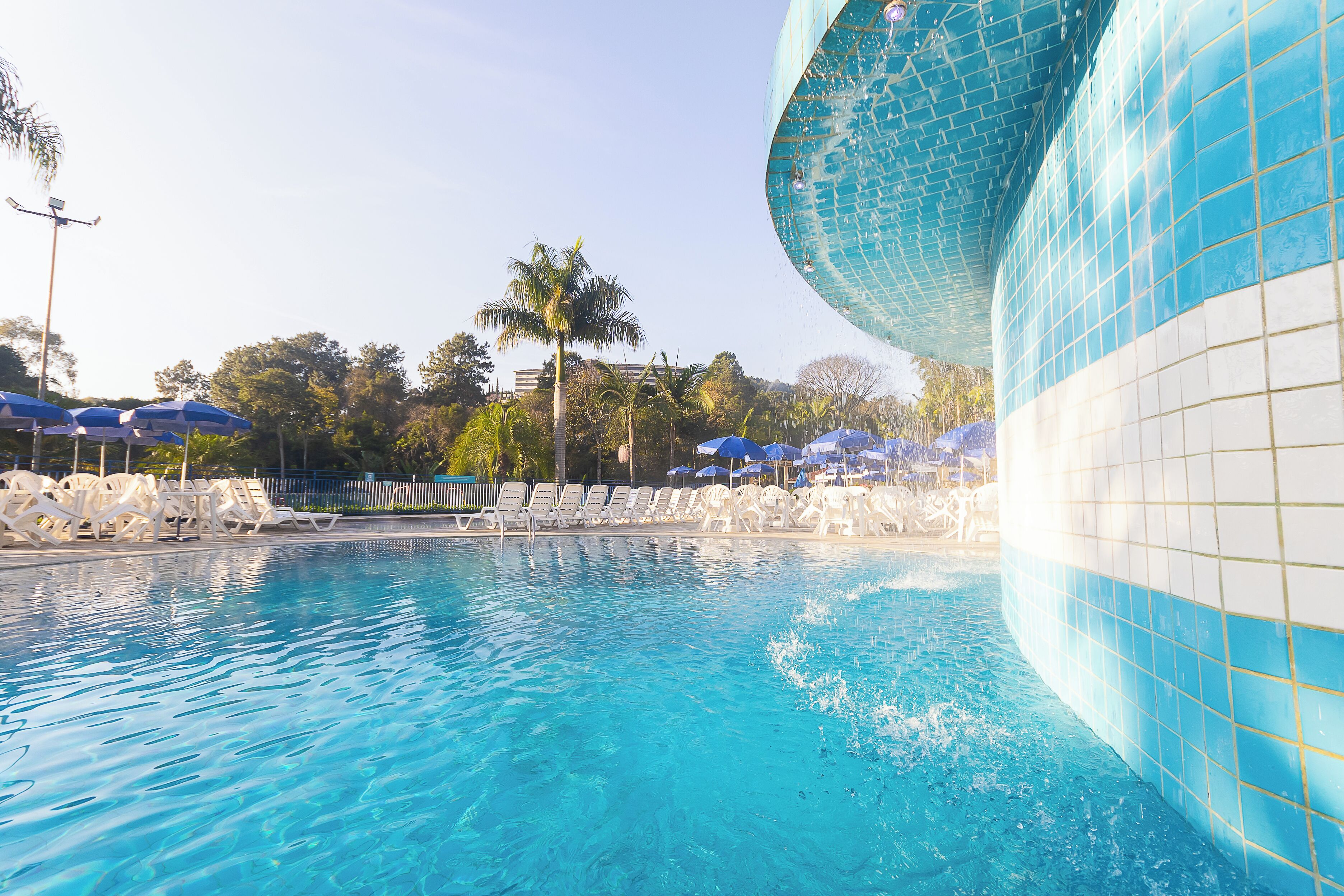 Une piscine à l’eau d’un bleu cristallin, entourée de chaises longues blanches et de parasols bleus.