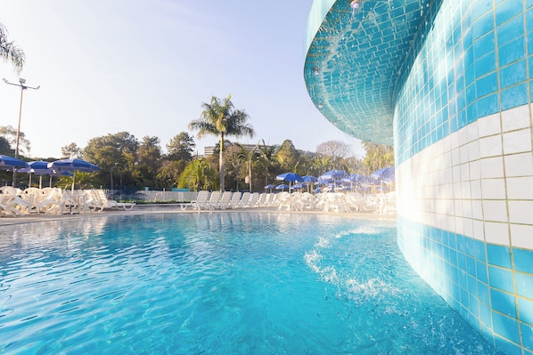 A swimming pool with clear blue water, surrounded by white lounge chairs and blue umbrellas. - Hotel Vilage Inn All Inclusive Poços de Caldas By Nacional Inn (Poços de Caldas)