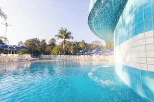 Piscina com água azul cristalina, cercada por cadeiras de descanso brancas e guarda-sóis azuis.