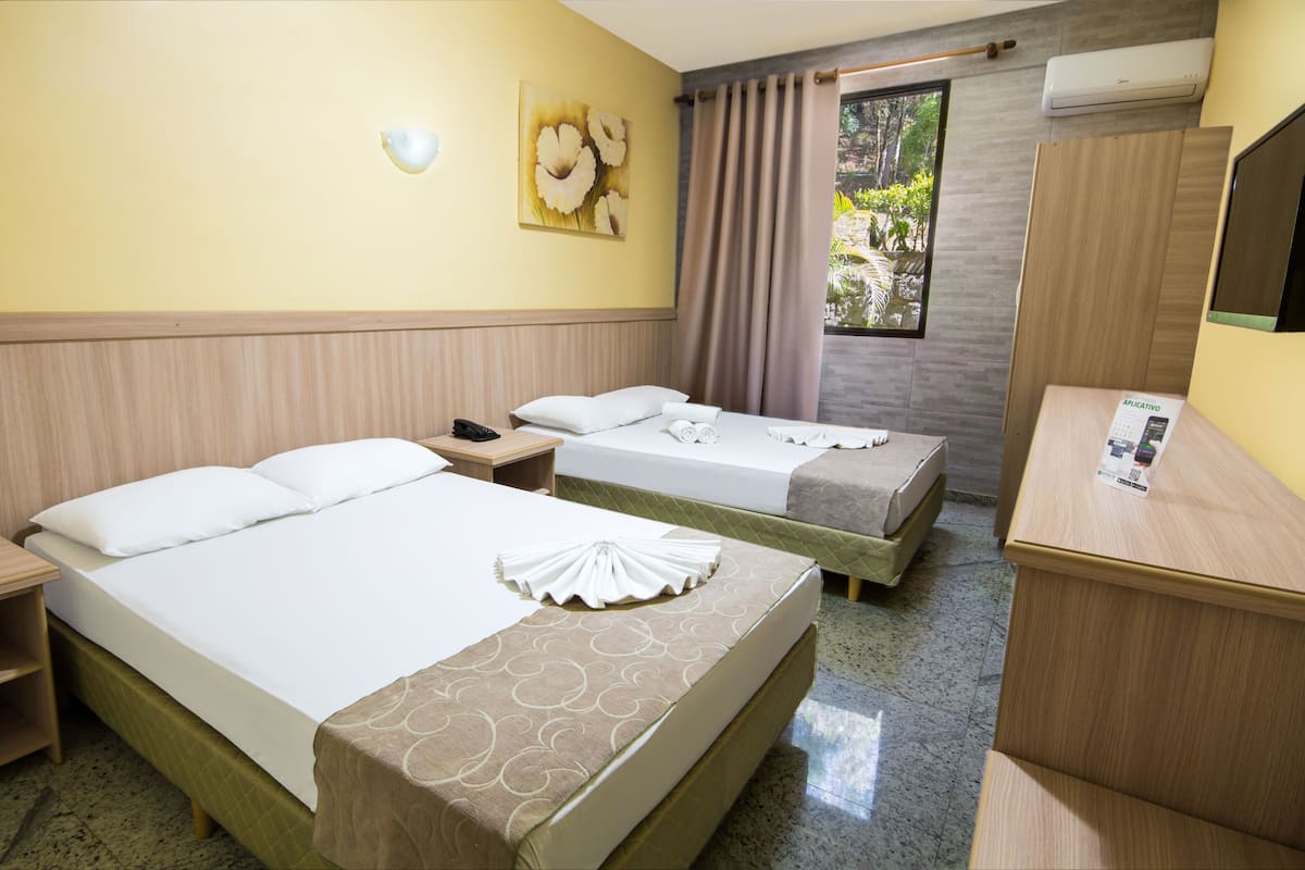 Quarto de hotel com duas camas, uma escrivaninha, um espelho e uma janela com cortinas.