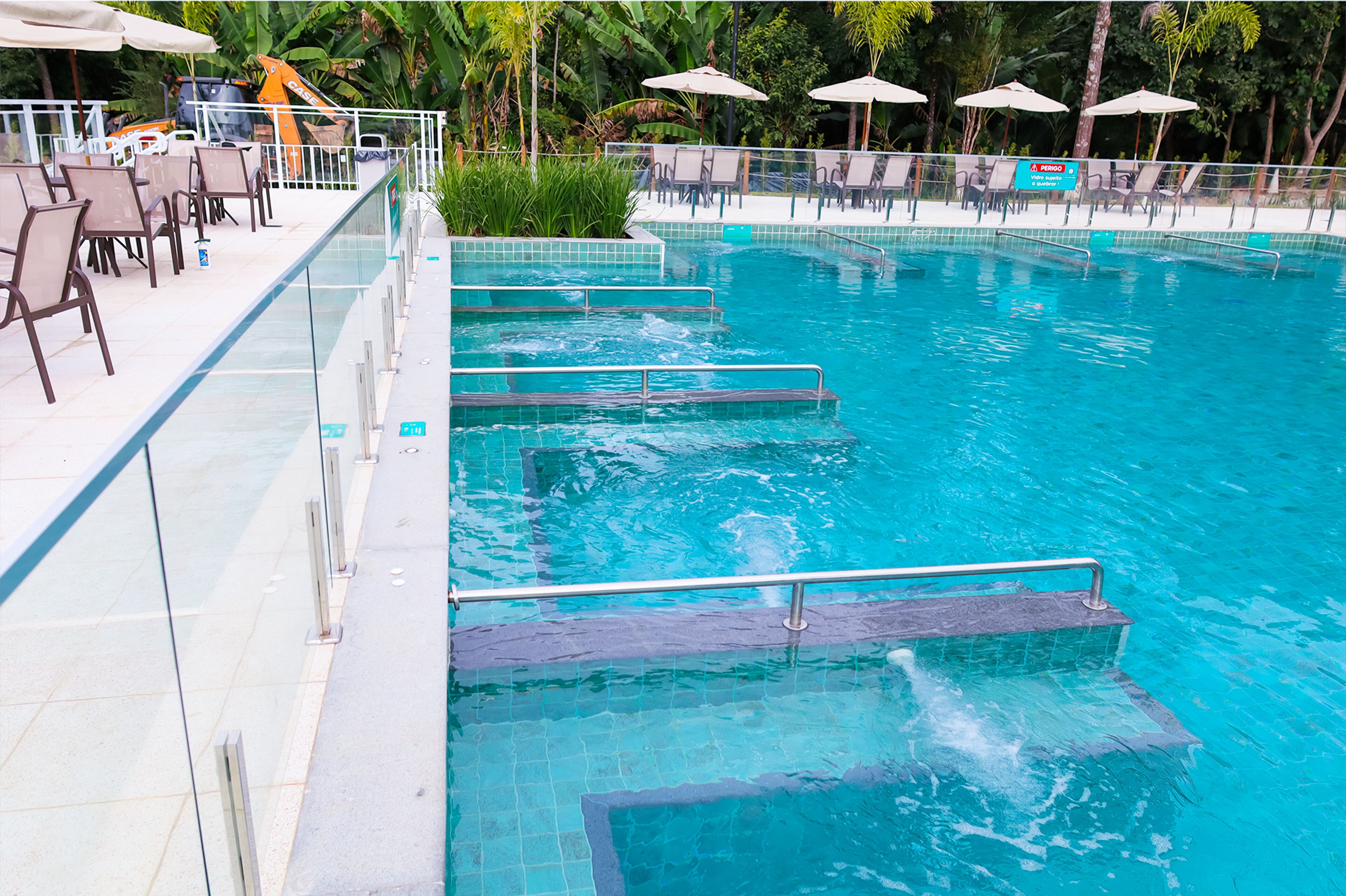 Una piscina con escalones de acceso, rodeada de sillas de descanso y sombrillas.