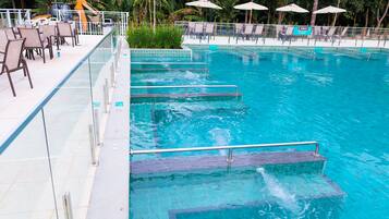Una piscina con escalones de acceso, rodeada de sillas de descanso y sombrillas.