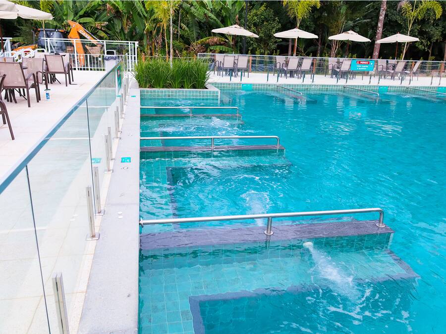 Una piscina con escalones de acceso, rodeada de sillas de descanso y sombrillas.