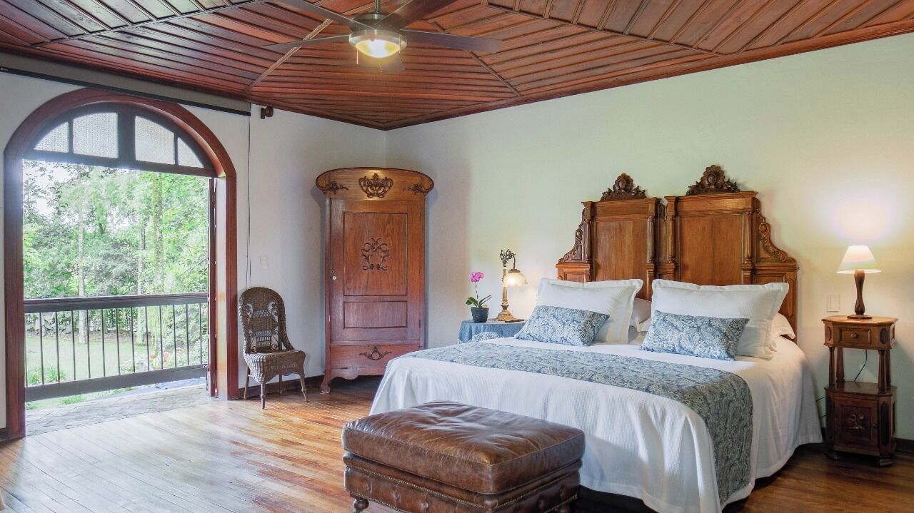 A bedroom with a large bed, wooden furniture, a chair, and a view of the outdoors.
