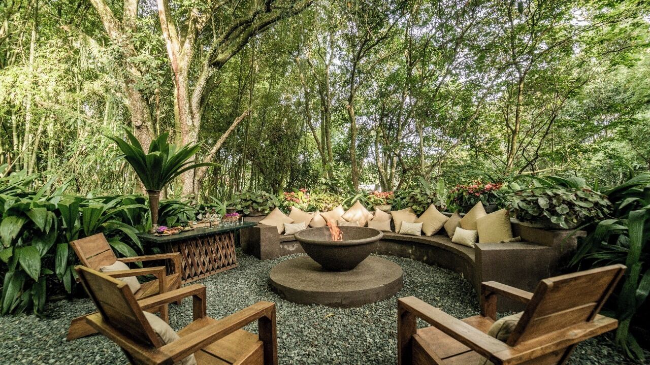 A circular seating area with a fire pit, surrounded by plants and trees.