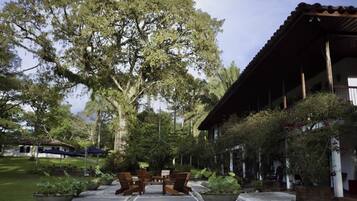Ein Gebäude mit überdachter Terrasse, Sitzgelegenheiten im Freien und einem großen Baum im Hintergrund.