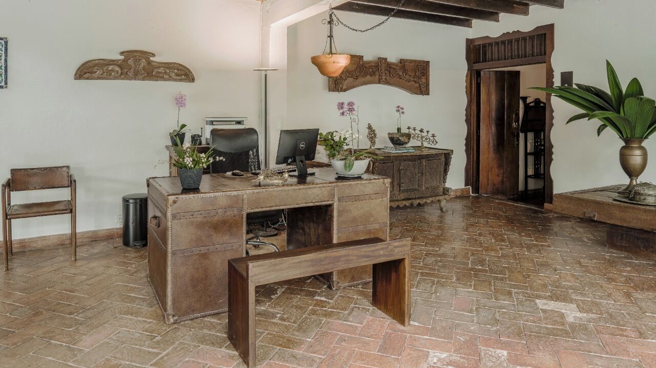 A rustic room with a wooden desk, a chair, a hanging light fixture, and a potted plant.