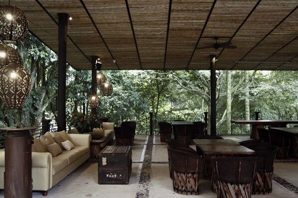 Un espacio de estar al aire libre con techo de madera, mobiliario de mimbre y lámparas colgantes.