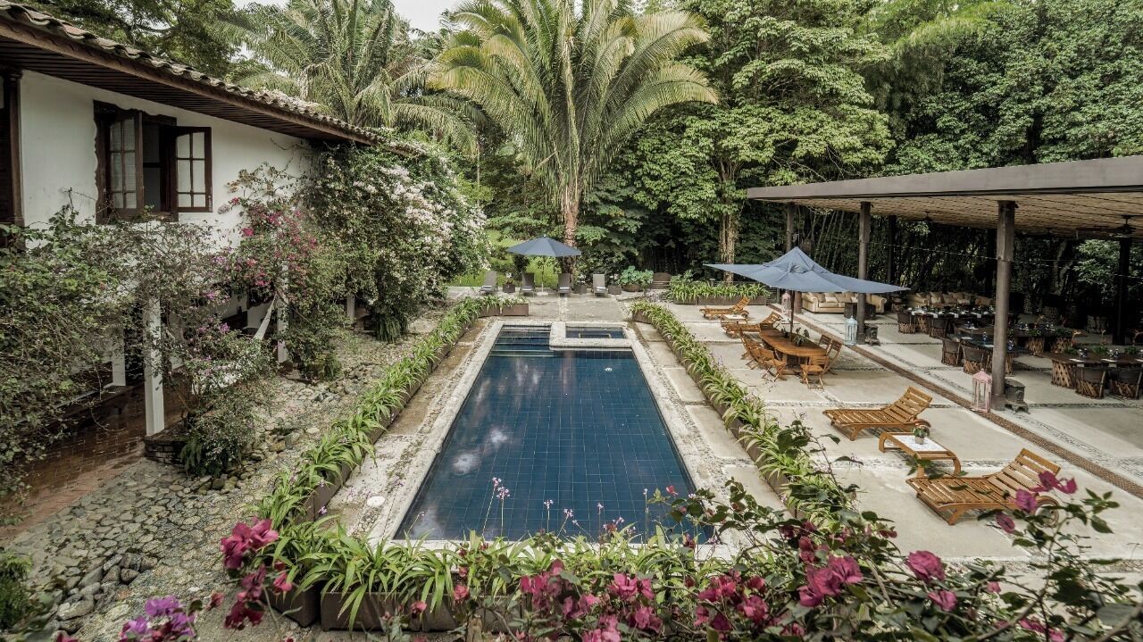 Ein Pool, umgeben von üppiger Vegetation, Holzliegen und einer überdachten Terrasse.