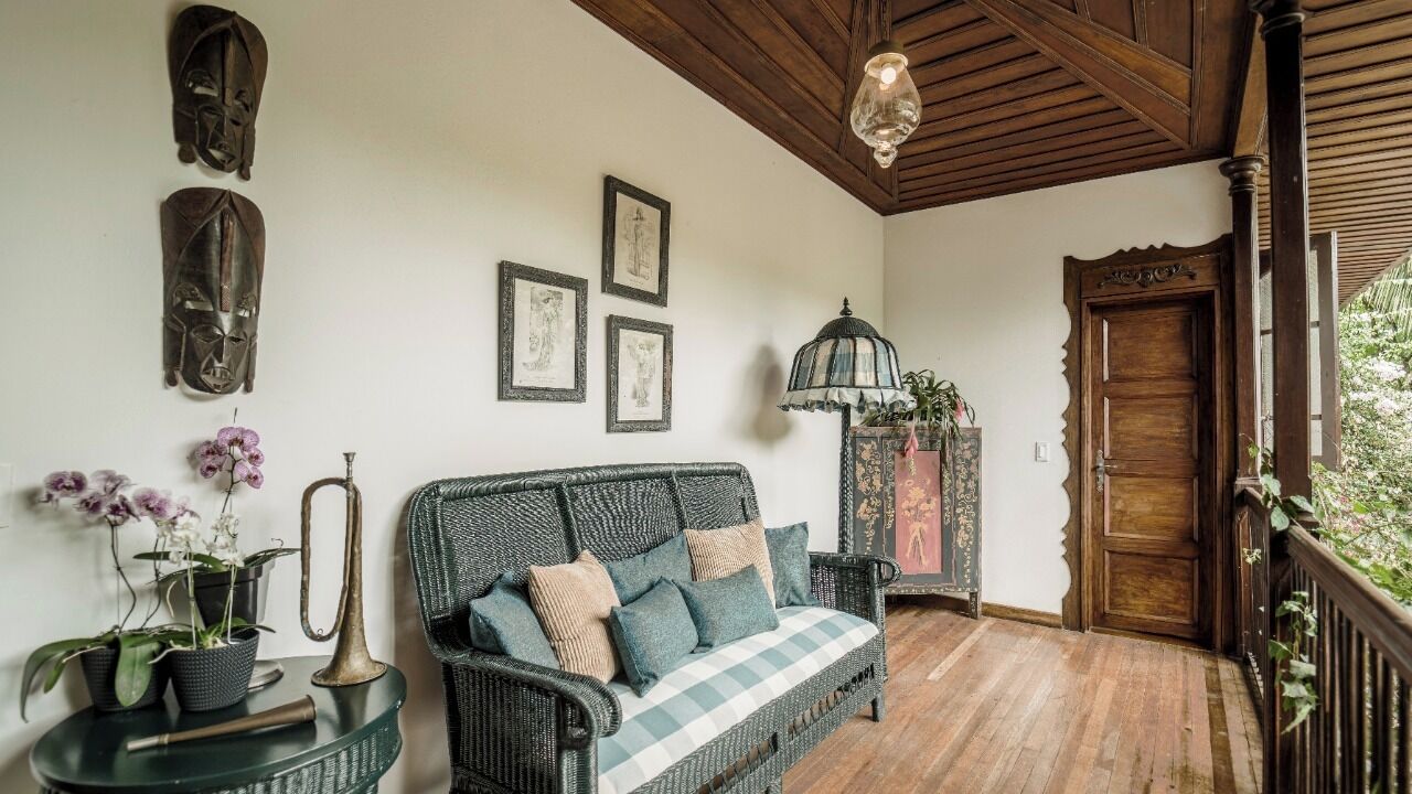 Une pièce chaleureuse avec un canapé en osier, des tableaux encadrés, une lampe et une porte en bois.