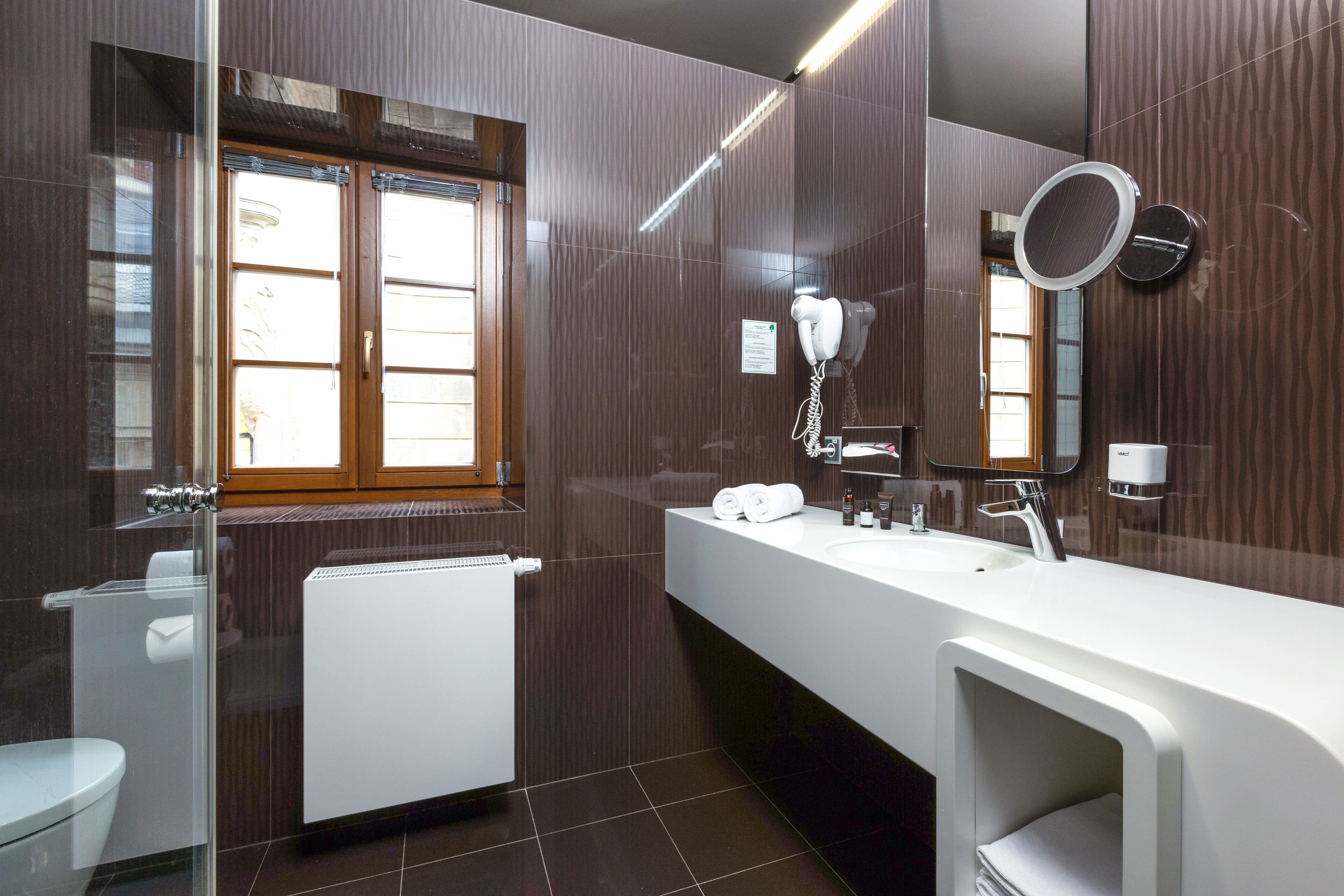 A modern bathroom with a large mirror, a white sink, and a toilet.