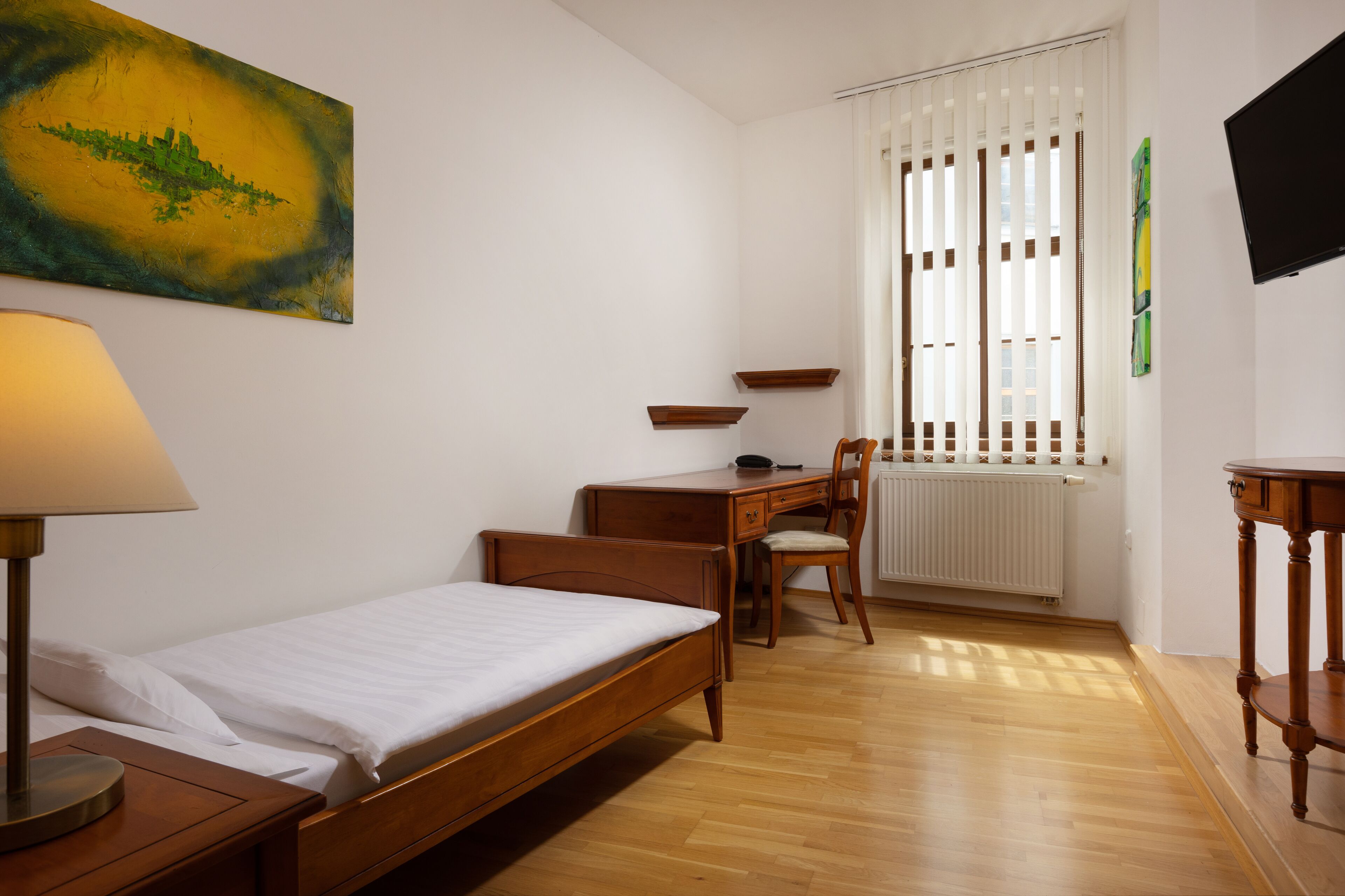 A bedroom with a single bed, a desk, a chair, a lamp, and a radiator.
