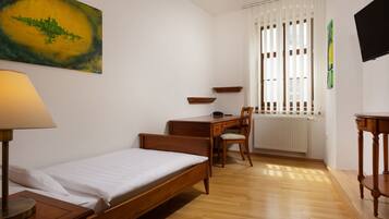 A bedroom with a single bed, a desk, a chair, a lamp, and a radiator.