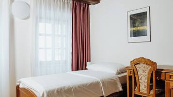 A bedroom with a wooden bed, a chair, a desk, and a window with curtains.