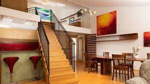 A spacious living area with a wooden staircase, a dining table with chairs, and a large abstract painting on the wall. - OREA Hotel Arigone Olomouc (Olomouc)