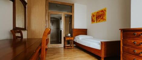 Un dormitorio con una cama de madera, un aparador, un escritorio y una silla. Hay una puerta que conduce a otra habitación.