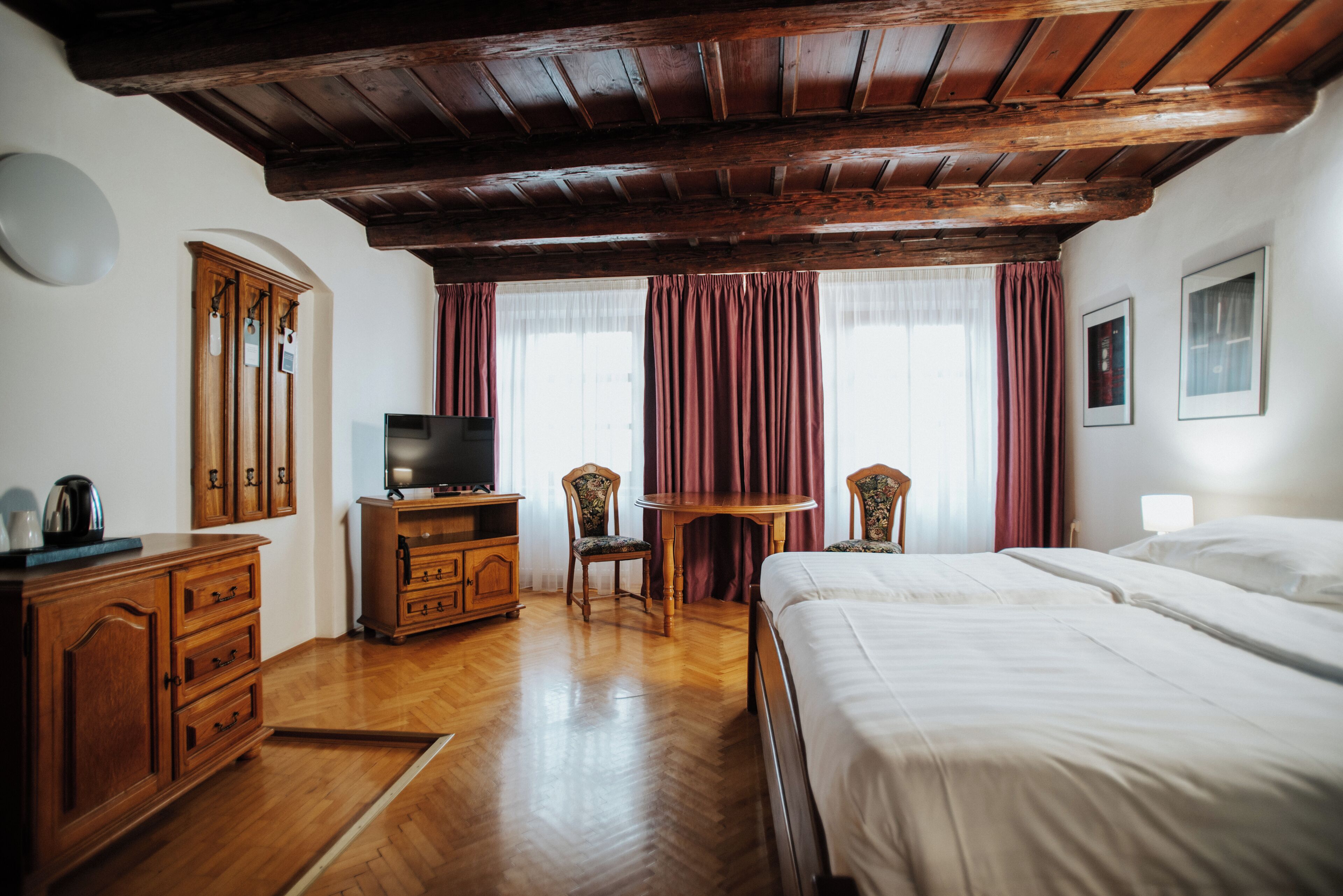 A hotel room with wooden flooring, a bed, a television, a desk, and two chairs.