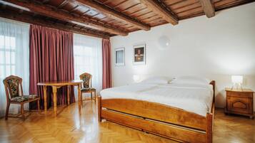 Quarto com cama de madeira, mesa de madeira, duas cadeiras e mesa de cabeceira com abajur.