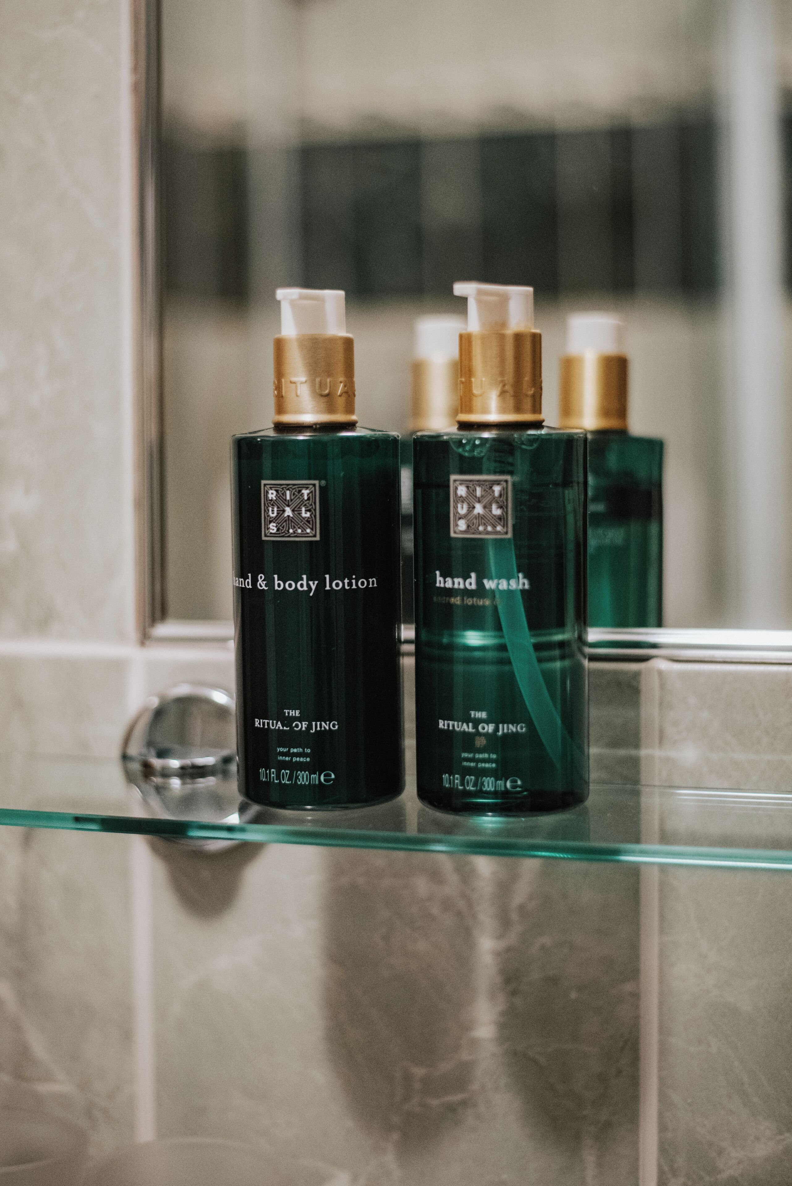 Dos botellas de loción para manos y cuerpo sobre un estante de vidrio en un baño.
