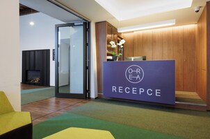 Un área de recepción con un mostrador de madera, alfombra verde y una puerta de vidrio que da a otra habitación.