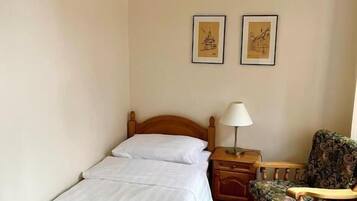 Une chambre à coucher avec un lit en bois, une table de chevet avec une lampe, une chaise et deux tableaux encadrés accrochés au mur.