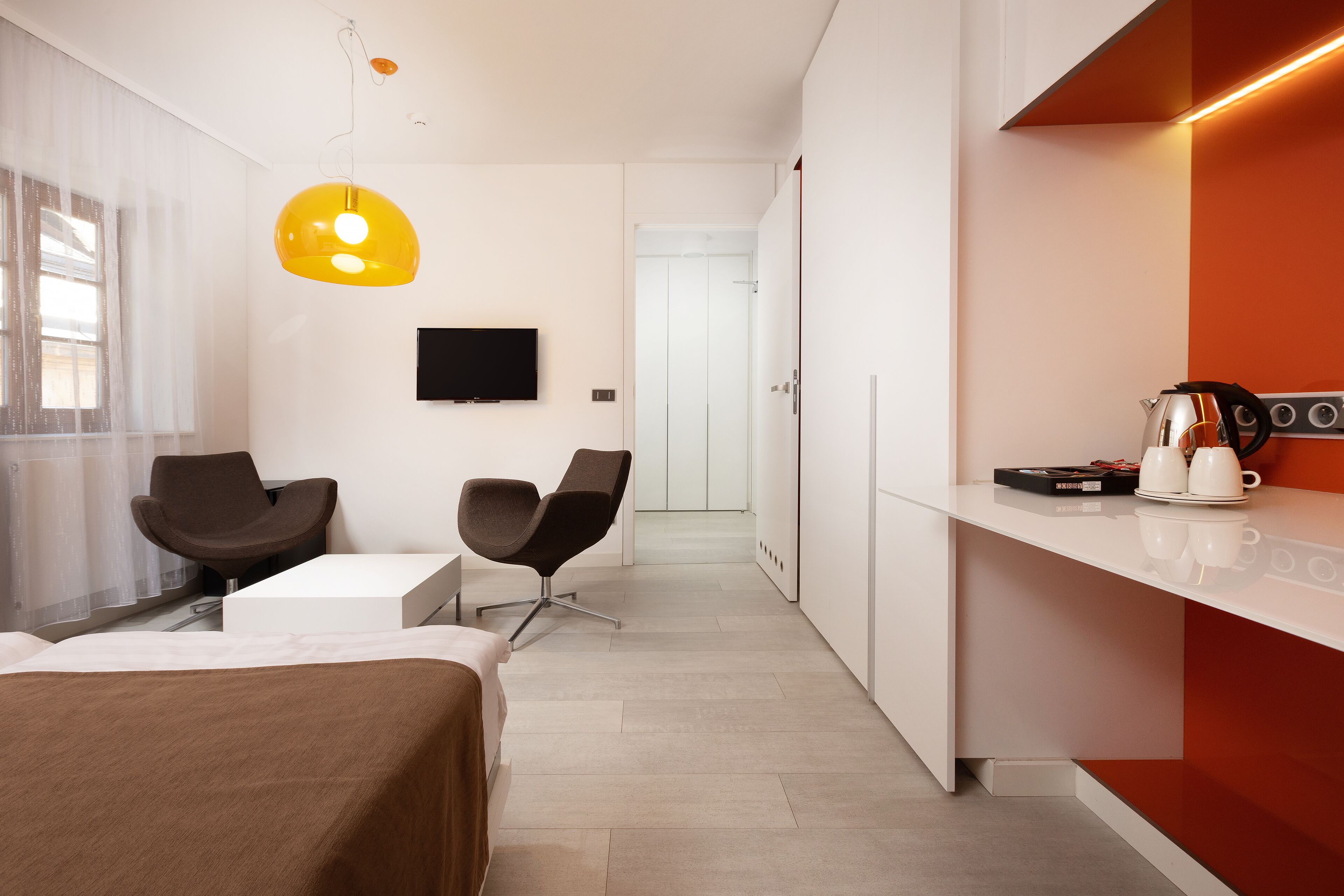 Habitación de hotel moderna con cama, dos sillas, televisor y kitchenette.
