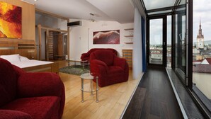 A modern hotel room with a large window, a red sofa, a small glass table, and a bed. - OREA Hotel Arigone Olomouc (Olomouc)
