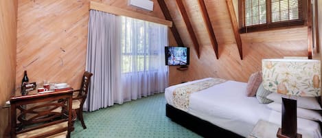 A cozy room with a bed, a TV, a table with a bottle and glasses, and a chair.