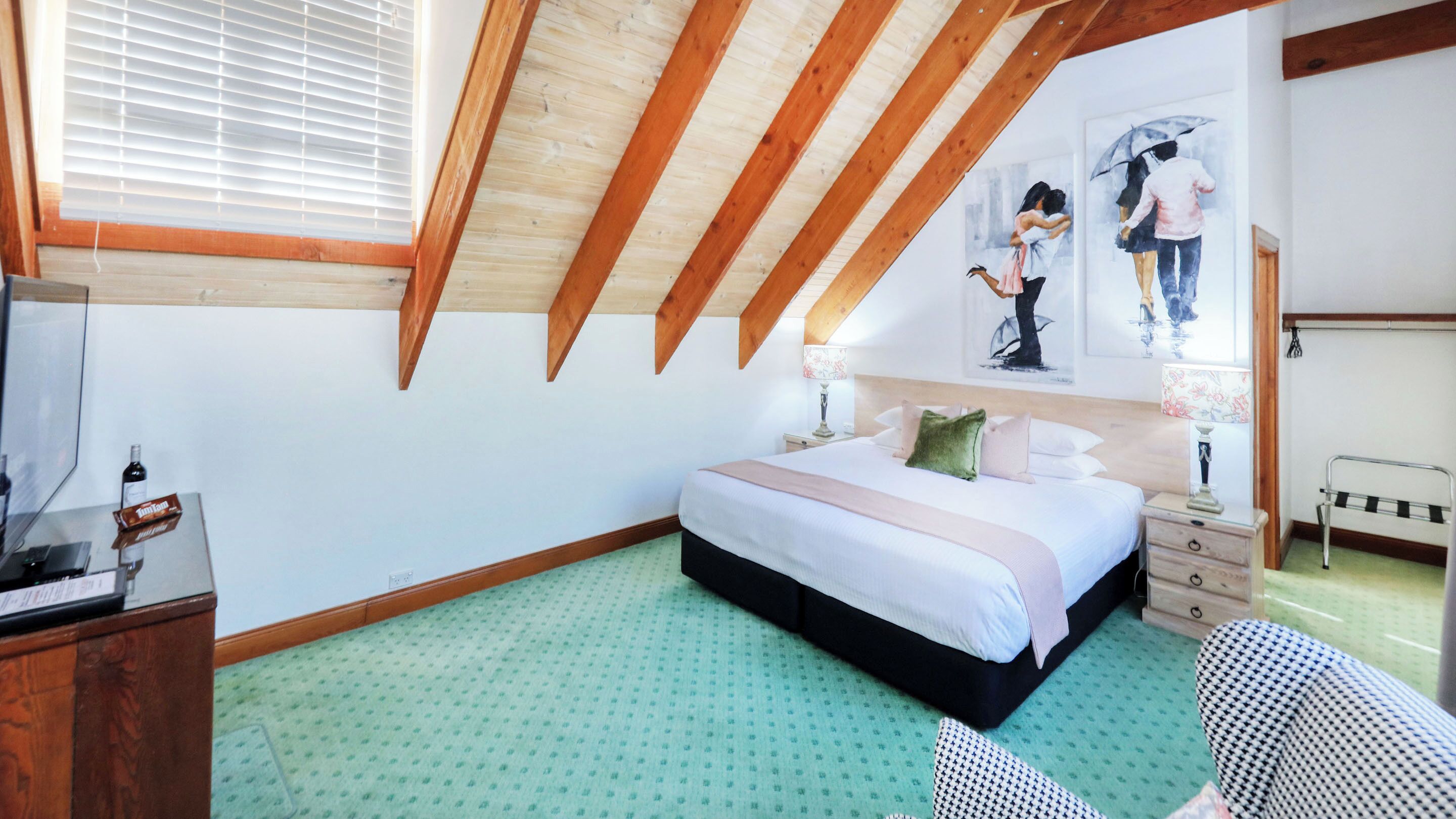 A bedroom with a sloped ceiling, a bed, a nightstand, a dresser, and artwork on the wall.