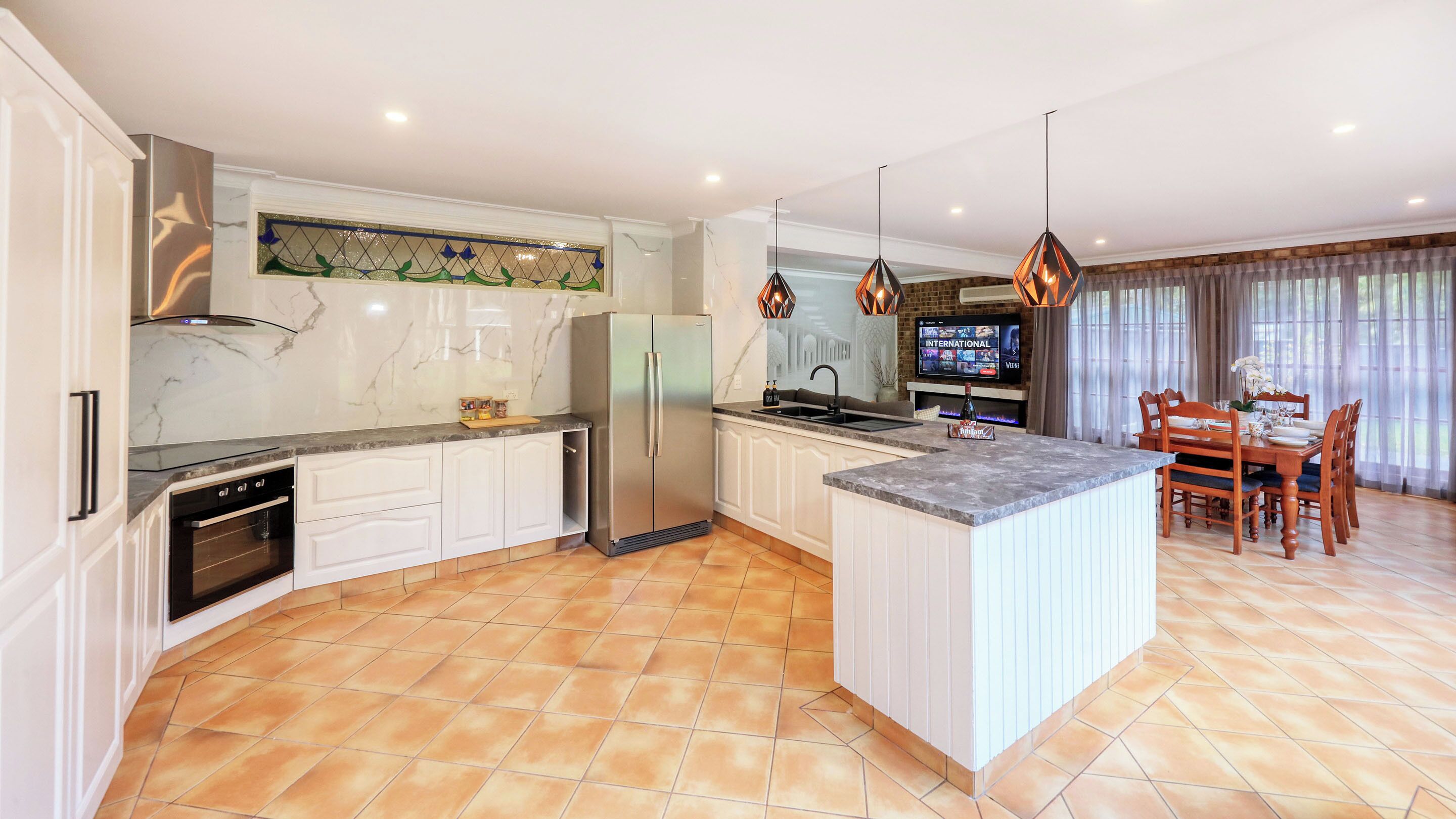 A modern kitchen with a central island, built-in oven, and a dining area with a TV.