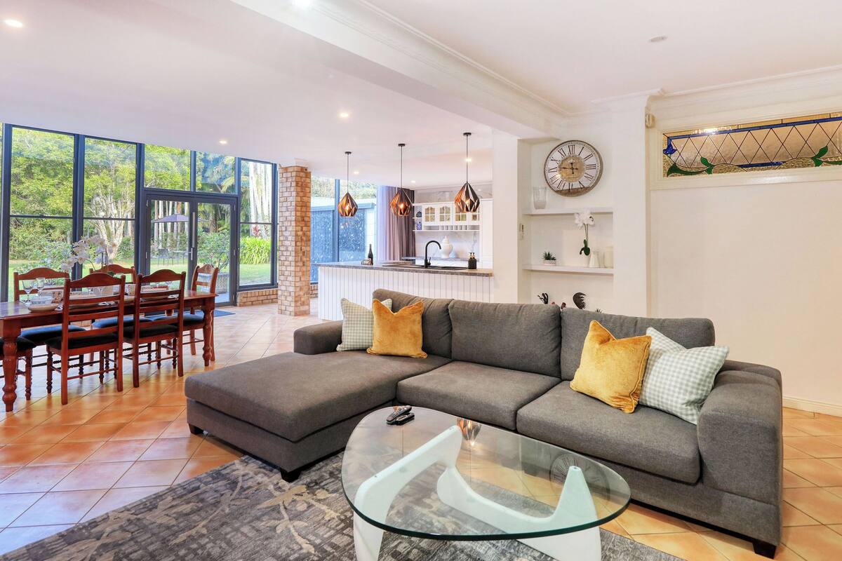 A spacious living room with a grey sectional sofa, a glass coffee table, and a dining area with wooden chairs and a table.