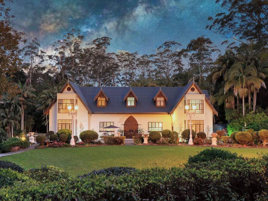 A large, two-story house with a symmetrical facade, multiple windows, and a well-maintained garden with various plants and a lawn.
