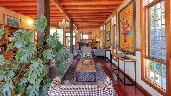 A cozy, well-lit room with wooden beams, a fireplace, and a large window with artwork. - Mt Tamborine Stonehaven Manor (Tamborine Mountain)