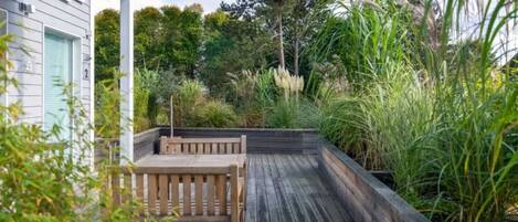 A wooden deck with a bench, surrounded by lush greenery and tall grasses.