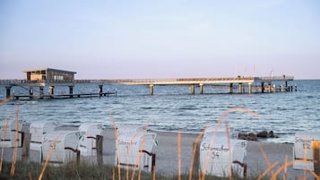 Un muelle que se adentra en el agua, con una torre de salvavidas y sillas de playa numeradas.