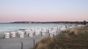 Una playa con hileras de buzones blancos numerados del 1 al 49, una orilla arenosa y un mar tranquilo.